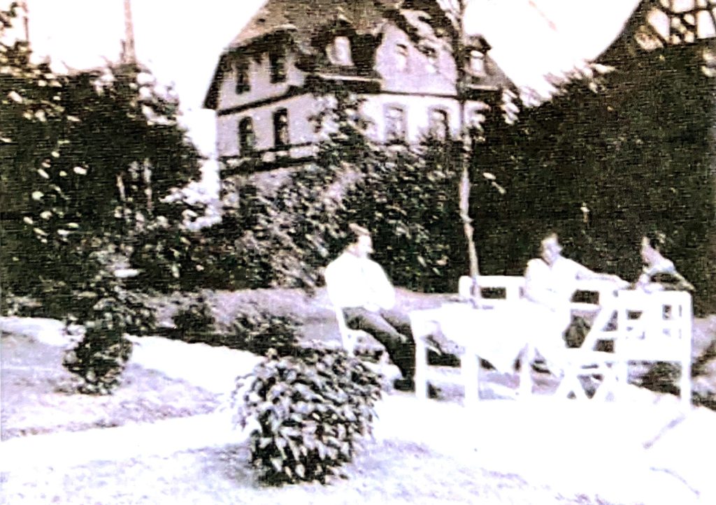 Verschwommenes schwarz-Weiß-Bild, das Menschen am Gartentisch zeigt. Der Tisch ist um einen dünnen Baum herum gebaut.